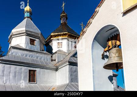 Un campanile è di fronte ad una chiesa con una campana appesa ad essa. Il campanile è alto e ha un tetto dorato. La chiesa è circondata da un bullo bianco Foto Stock