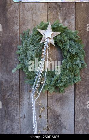 Corona di Natale in rami di abete con stella decorativa e nastri su una parete di legno. Atmosfera natalizia rustica, Muensterland, Renania settentrionale-Westph Foto Stock