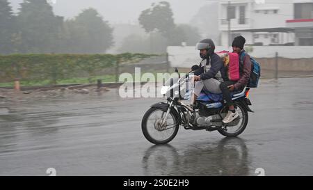 Beawar, Rajasthan, India, 27 dicembre 2024: Pendolari in una strada in mezzo alla pioggia la mattina d'inverno a Beawar. La vita quotidiana nel Rajasthan è stata gravemente colpita dalla pioggia e dalla nebbia che hanno colpito lo stato, portando a un brusco calo delle temperature e a una ridotta visibilità in diverse aree. Il tempo inclemente ha intensificato il freddo, con una fitta nebbia che ricopre molte regioni. L'India Meteorological Department (IMD) ha emesso un allarme arancione per 15 distretti e un allarme giallo per sei distretti nello stato, avvertendo della persistente nebbia densa nei prossimi tre giorni. Crediti: Sumit Saraswat / Alamy Live ne Foto Stock