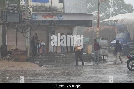 Beawar, Rajasthan, India, 27 dicembre 2024: Le persone si spostano lungo una strada in mezzo alla pioggia la mattina d'inverno a Beawar. La vita quotidiana nel Rajasthan è stata gravemente colpita dalla pioggia e dalla nebbia che hanno colpito lo stato, portando a un brusco calo delle temperature e a una ridotta visibilità in diverse aree. Il tempo inclemente ha intensificato il freddo, con una fitta nebbia che ricopre molte regioni. L'India Meteorological Department (IMD) ha emesso un allarme arancione per 15 distretti e un allarme giallo per sei distretti nello stato, avvertendo della persistente nebbia densa nei prossimi tre giorni. Crediti: Sumit Saraswat / Alamy Live ne Foto Stock