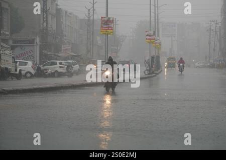 Beawar, Rajasthan, India, 27 dicembre 2024: Pendolari in una strada in mezzo alla pioggia la mattina d'inverno a Beawar. La vita quotidiana nel Rajasthan è stata gravemente colpita dalla pioggia e dalla nebbia che hanno colpito lo stato, portando a un brusco calo delle temperature e a una ridotta visibilità in diverse aree. Il tempo inclemente ha intensificato il freddo, con una fitta nebbia che ricopre molte regioni. L'India Meteorological Department (IMD) ha emesso un allarme arancione per 15 distretti e un allarme giallo per sei distretti nello stato, avvertendo della persistente nebbia densa nei prossimi tre giorni. Crediti: Sumit Saraswat / Alamy Live ne Foto Stock