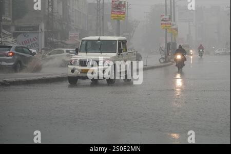 Beawar, Rajasthan, India, 27 dicembre 2024: I veicoli attraversano strade bagnate in mezzo alla pioggia la mattina d'inverno a Beawar. La vita quotidiana nel Rajasthan è stata gravemente colpita dalla pioggia e dalla nebbia che hanno colpito lo stato, portando a un brusco calo delle temperature e a una ridotta visibilità in diverse aree. Il tempo inclemente ha intensificato il freddo, con una fitta nebbia che ricopre molte regioni. L'India Meteorological Department (IMD) ha emesso un allarme arancione per 15 distretti e un allarme giallo per sei distretti nello stato, avvertendo della persistente nebbia densa nei prossimi tre giorni. Crediti: Sumit Saraswat / Alam Foto Stock