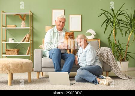 Felice coppia anziana con un carino cane della Pomerania e un portatile che riposano a casa Foto Stock