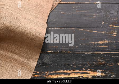 Pezzo di tessuto burlap su sfondo in legno nero Foto Stock