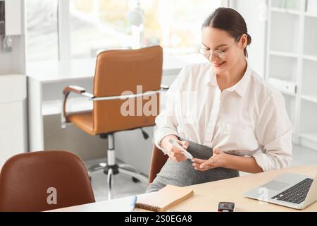 Giovane donna d'affari incinta con diabete gestazionale che utilizza una penna a lancetta in ufficio Foto Stock