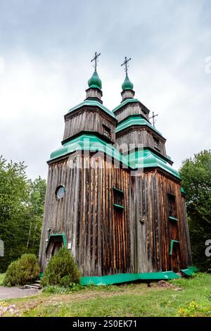 Una grande chiesa in legno con due cupole verdi in cima. La chiesa è circondata da alberi e erba Foto Stock