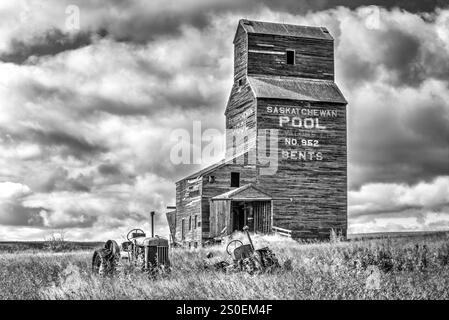 Una foto in bianco e nero di un'azienda agricola con un silo di grano grande e un paio di vecchi trattori Foto Stock