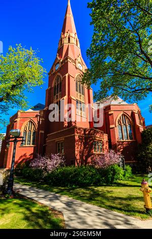 Una grande chiesa in mattoni rossi con un campanile e una croce in cima. La chiesa è circondata da alberi e ha un idrante giallo nell'erba Foto Stock