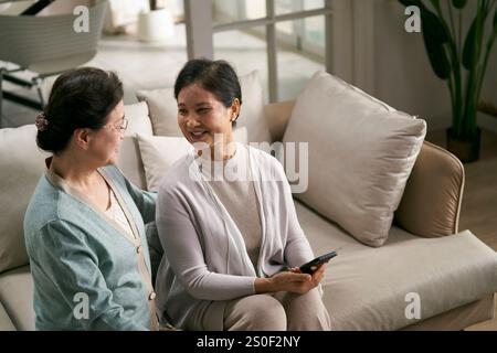 due donne asiatiche anziane felici sedute sul divano di famiglia che fanno una piacevole conversazione Foto Stock
