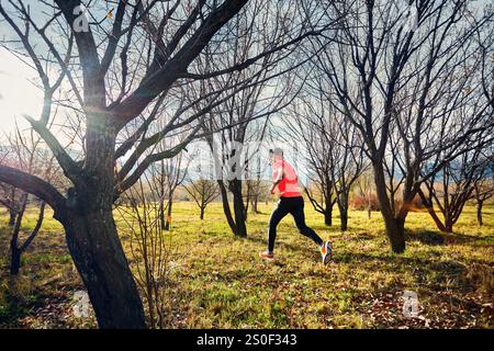 Atletico barbuto in camicia rossa che corre sul sentiero nella foresta autunnale all'alba Foto Stock