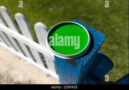 Coperchio della lattina di vernice verde appoggiato sul palo della recinzione. Dipingere una recinzione di legno con vernice acrilica Foto Stock