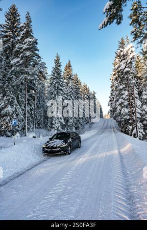 Un tranquillo e sereno paesaggio innevato mostra un veicolo che scivola su una strada innevata, avvolto da alti pini Foto Stock