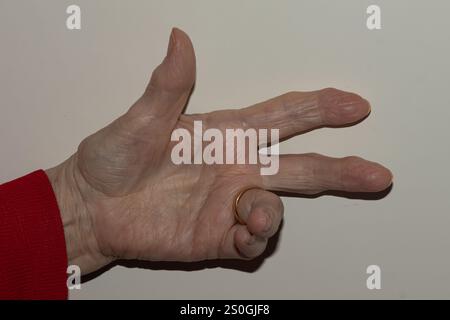 Vista ravvicinata della mano di una donna anziana che mostra il numero tre, sottolineando le texture della pelle invecchiate e un semplice sfondo Foto Stock