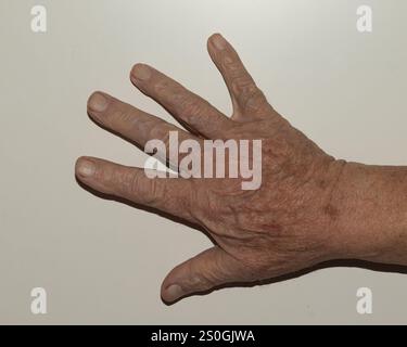 Immagine ravvicinata di una mano anziana completamente aperta con tutte e cinque le dita allungate, appoggiata su uno sfondo semplice. Questo gesto rappresenta in genere il numero Foto Stock
