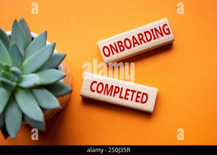 Simbolo onboarding completato. Termine concettuale onboarding completato su blocchi di legno. Bellissimo sfondo arancione con piante succulente. Affari e Onboar Foto Stock