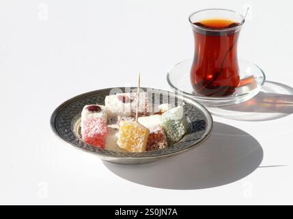 Varietà di delizie turche aka Lokum e un bicchiere di tè turco isolato su bianco Foto Stock