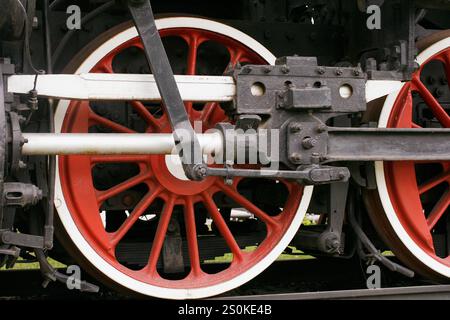 Vista ravvicinata dettagliata che mostra le vibranti ruote rosse a raggi e gli intricati componenti meccanici di un treno d'epoca, catturando la precisione e l'histo Foto Stock