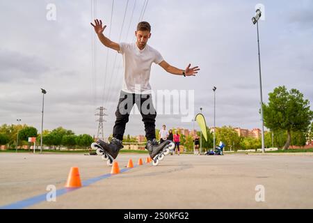 Uomo che salta su rollerblade mentre naviga nei coni in un parco Foto Stock