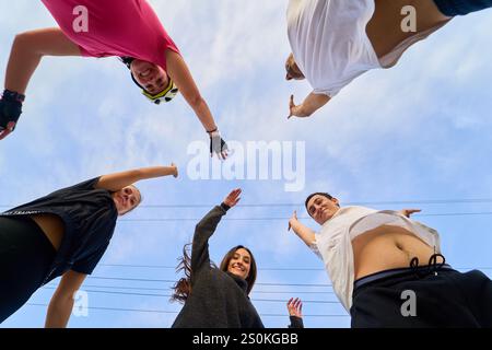 Gruppo di pattinatori che festeggiano con le braccia alzate, visto dal basso Foto Stock