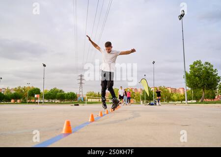 Uomo che salta su rollerblade mentre naviga nei coni in un parco Foto Stock