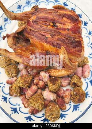 Primo piano di un tacchino tostato al forno con croccanti strisce di pancetta sopra, appoggiato su un ampio piatto di portata, con polpette ripiene e salsicce. Foto Stock