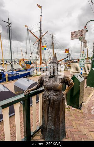 Barche a vela e statua in bronzo di una donna in costume tradizionale nel porto di Volendam, Olanda, Paesi Bassi. Foto Stock