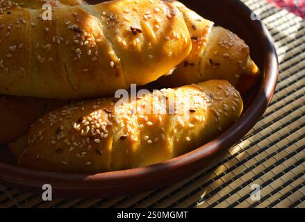 Hot dog nell'impasto su un piatto di ceramica, sotto i raggi del sole. Deliziosi pasticcini per cena. Salsicce fatte in casa con impasto. Foto Stock