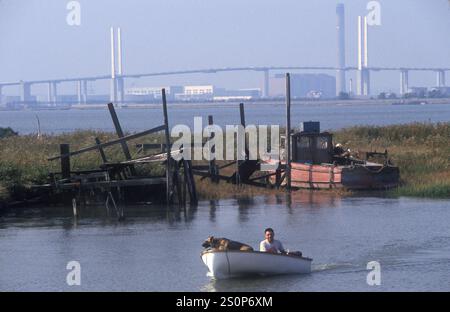 Penisola di Swanscombe, nel nord del Kent. Fuori rete che vive una comunità di persone a Broadness Creek. Uomo il suo cane e la sua barca che vivono uno stile di vita alternativo. Borough of Dartford Inghilterra Dartford Bridge.1991 1990s Regno Unito Dartford Bridge attraversamento in lontananza. HOMER SYKES. Foto Stock