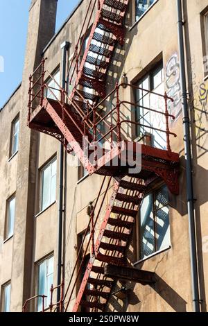 Esterno urbano di un vecchio edificio con una fuga antincendio in metallo rosso che conduce al tetto, con finestre e graffiti visibili sulle pareti manchester uk Foto Stock