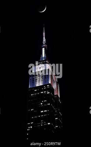 L'Empire State Building si illumina di rosso, bianco e blu di notte con una mezzaluna sopra la testa Foto Stock