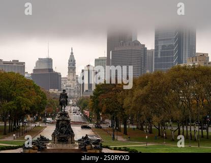 Una vista nebbiosa dello skyline della città con alti edifici e una statua in primo piano. L'atmosfera è allegra con cieli ricoperti, che mostrano l'autunno Foto Stock