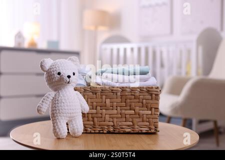 Cestino in vimini con pila di vestiti per bambini e orsacchiotto sul tavolino da caffè all'interno, primo piano Foto Stock