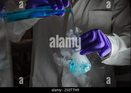 Una donna scienziata che esegue una reazione organica in condizioni di fumatura in laboratorio. Fumi, radioattivi, fluorescenza. Uno spazio di copia su sfondo nero. Foto Stock