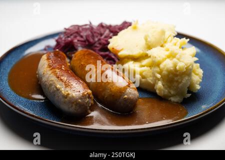 , Deutschland, 29.12.2024, Bratwürste mit dunkler Soße, Rotkohl und cremigem Kartoffelpüree auf einem blauen Teller – ein klassisches deutsches Geric Foto Stock