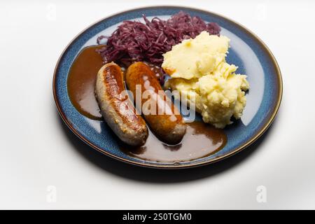 , Deutschland, 29.12.2024, Bratwürste mit dunkler Soße, Rotkohl und cremigem Kartoffelpüree auf einem blauen Teller – ein klassisches deutsches Geric Foto Stock