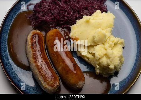 Traditionelles Gericht mit Bratwurst und Beilagen , Deutschland, 29.12.2024, Bratwürste mit dunkler Soße, Rotkohl und cremigem Kartoffelpüree auf einem blauen Teller ein klassisches deutsches Gericht. *** Piatto tradizionale con bratwurst e contorni , Germania, 29 12 2024, bratwurst con salsa scura, cavolo rosso e crema di patate su un piatto blu un classico piatto tedesco Foto Stock