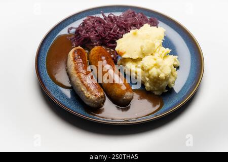 Traditionelles Gericht mit Bratwurst und Beilagen , Deutschland, 29.12.2024, Bratwürste mit dunkler Soße, Rotkohl und cremigem Kartoffelpüree auf einem blauen Teller ein klassisches deutsches Gericht. *** Piatto tradizionale con bratwurst e contorni , Germania, 29 12 2024, bratwurst con salsa scura, cavolo rosso e crema di patate su un piatto blu un classico piatto tedesco Foto Stock