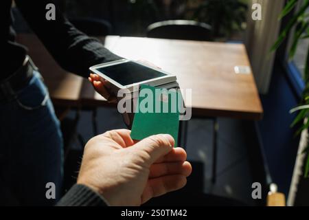 Un uomo accetta pagamenti da un cliente tramite un terminale di carta di credito in un negozio o in un bar, Foto Stock