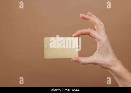 A mano con carta di credito dorata su sfondo dorato beige. Foto Stock