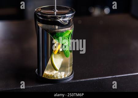 tè tonico vitaminico con limone, zenzero e menta, su sfondo scuro in una teiera trasparente, Foto Stock
