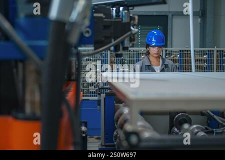 Ingegnere donna indiana con casco blu e occhiali di sicurezza, funzionamento di un pannello di controllo, controllo e automazione dei processi industriali. Foto Stock