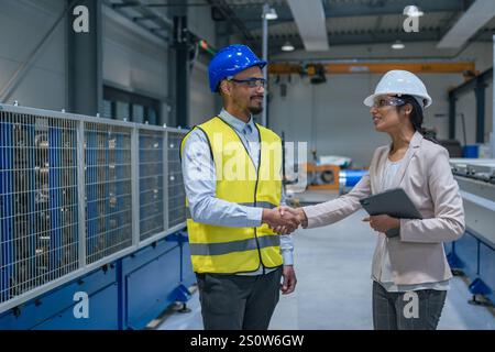 Il manager ingegnere donna che indossa un elmetto di sicurezza sta addestrando il lavoratore del settore nella fabbrica di produzione. Foto Stock
