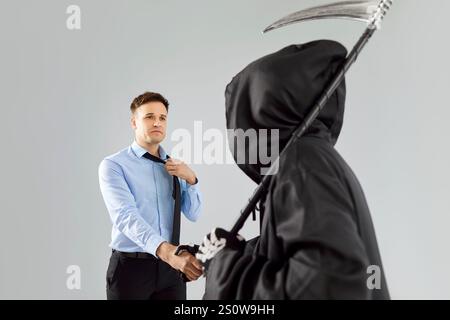 Giovane uomo d'affari turbato che stringe mano facendo un patto con il diavolo su sfondo grigio studio. Foto Stock