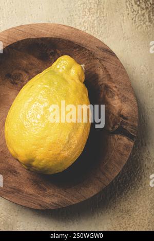 Un vibrante limone giallo siede in cima a un piatto rustico di legno, che mostra la sua consistenza sconnessa e il colore luminoso su uno sfondo delicatamente illuminato, Highlig Foto Stock