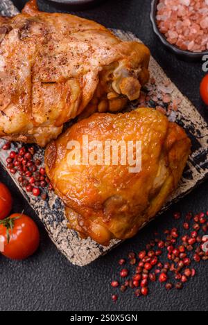 Deliziose cosce di pollo succose cotte con sale, spezie ed erbe in un piatto di ceramica su fondo di cemento scuro Foto Stock