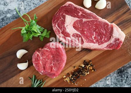 La bistecca cruda taglia con erbe, aglio e spezie su un asse di legno. Foto Stock