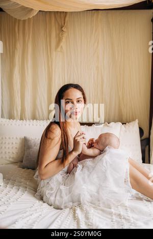 Madre che tiene il bambino in una camera da letto serena, caratterizzata da toni morbidi e neutri Foto Stock