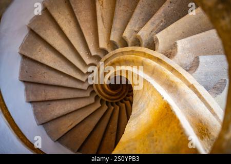 Una stupenda scala elicoidale scorre verso il basso, mostrando intricati lavori in pietra e una calda tonalità dorata. Il design cattura un senso di movimento ed eleganza in un'atmosfera invitante. Foto Stock