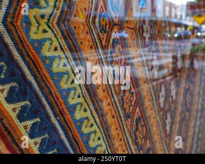 Un arazzo colorato intrecciato a mano con intricati motivi geometrici riflette l'ambiente urbano in una vetrina, mescolando arte tradizionale con un moderno c Foto Stock