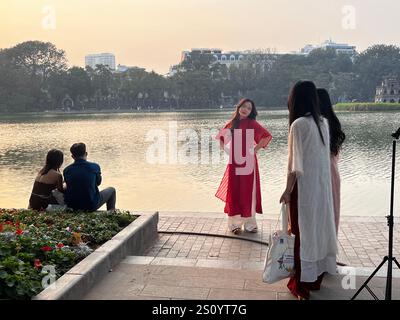 Una donna in abito tradizionale posa per un servizio fotografico al tramonto presso il lago Hoan Kiem, catturando un momento sereno di Hanoi. Foto Stock